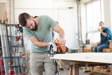 young worker in a carpenter's workshop with hand saw