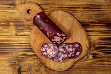Sliced salami sausage on cutting board on wooden table. Top view