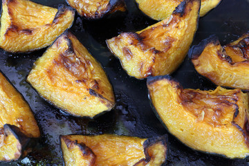 A close view of some orange roasted and crunchy pumpkin slices cooked in an oven over a black glass surface, with black edges