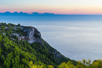 Fototapeta na wymiar Greece, Zakynthos, Endless silent blue ocean behind green tree covered chalk cliff in evening twilight