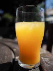 Pint glass full of orange juice on a hot day, on a wooden table