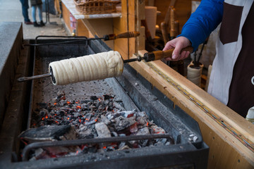 Kurtos kalacs (Chimney Cakes) baking on roll spinning over hot coals at a Christmas market stand.Chimney cakes baked over an open charcoal grill