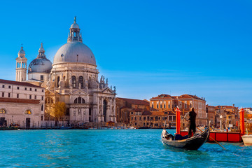 Fototapeta premium Kurtka w paski Gondolier jest na wiosłach błękitnej rzeki w Wenecji, przykład starożytnej architektury z kilkoma szarymi kopułami