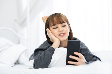 Beautiful Attractive Asian woman lying on white bed using smartphone using social media in bedroom smile and happiness with social media and shopping online,Lifestyle in Holidays Concept