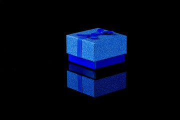 Obraz premium Blue luxury present box isolated on a black glossy background with reflection.- Image