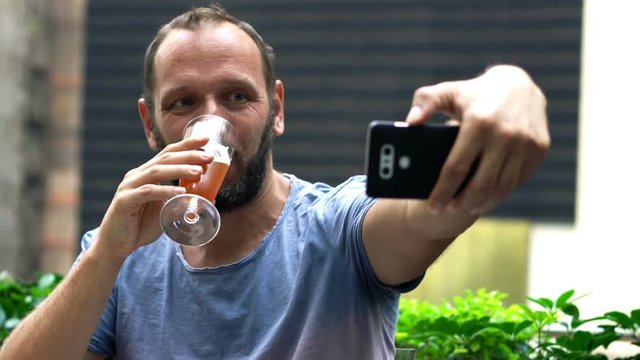 Happy man with beer taking selfie photo with cellphone on terrace in bar