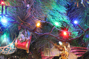 A close view of a green leaves Christmas tree with electric lights decorations, hanging ornaments and baubles in a bright colored atmosphere