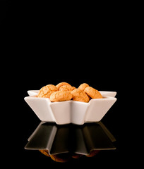 Amaretti traditional italian almond cookies. Christmas & new year cookies amaretti in a white star shaped bowl on a black glossy background with reflection.- Image