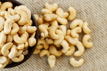 Cashew nuts in a wooden bowl on a burlap cloth background.