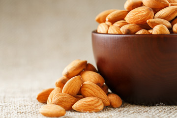 Almonds in a wooden cup on a burlap cloth background.