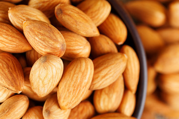 Almonds in a wooden cup on a burlap cloth background.