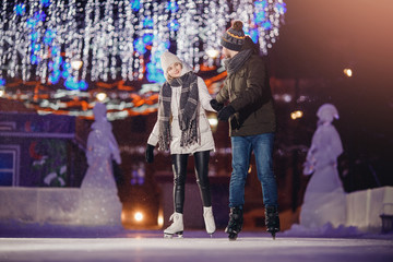 Winter skates, loving couple holding hands and rolling on rink. Illumination in background, night. Concept training