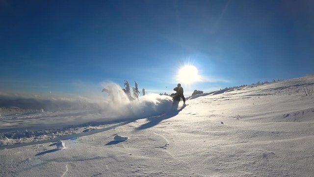 the guy on the snowmobile tearing fresh snow leaving the mountains. makes a turn with a whirlwind of snow. opposite the bright sun. on the background of beautiful firs covered with snow. super slowmo