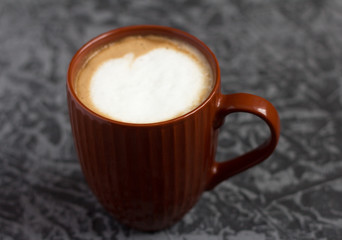 hot cappuccino coffee in a brown mug on a gray background