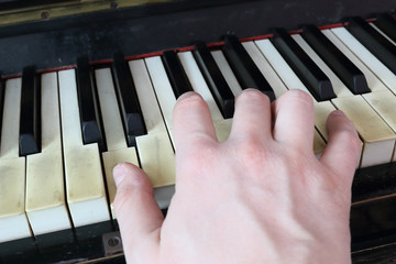A right hand playing a D (RE) major chord on an old black piano with yellowed cracked keys, pressing the D (RE), F# diesis (FA#), A (LA) notes