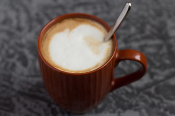 hot cappuccino coffee in a brown mug on a gray background