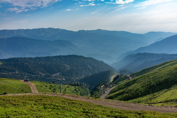 The cable car goes down from the green ridge Aibga. High mountains in the haze on the horizon. Krasnaya Polyana, Sochi, Caucasus, Russia.