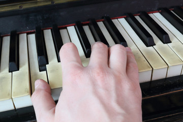 A right hand playing a C (DO) major chord on an old black piano with yellowed cracked keys, pressing the C (DO), E (MI), G (SOL) notes