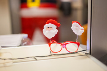horizontal image with detail of a pair of red glasses decorated with Christmas puppets, laid on a...