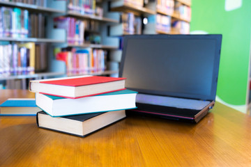 Book and laptop stack on desk and blurred bookshelf in the library room. Educate background, back to school concept.