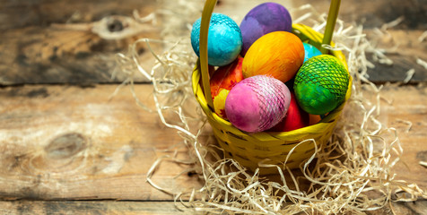 beautiful, bright, colorful hand-painted Easter eggs in a yellow basket on a natural, wooden background