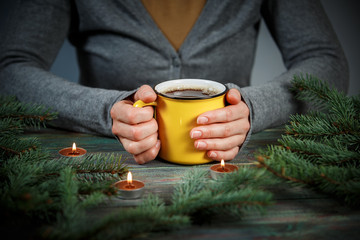 Fototapeta na wymiar Woman holds a cup of hot tea among the fir branches and candle.