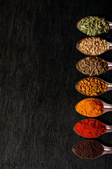 spices in spoons on black background