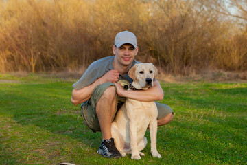 Young guy with labrador on walk in summer park. Educating dog. Play with a pet. Dog handler