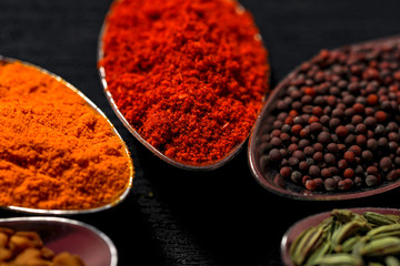 spices in spoons on black background