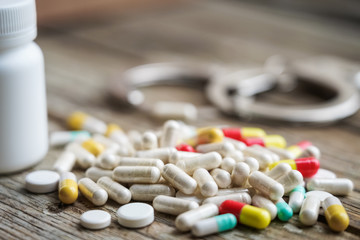 Handcuffs and pills and drugs on wooden table.