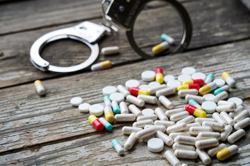 Handcuffs and pills and drugs on wooden table.