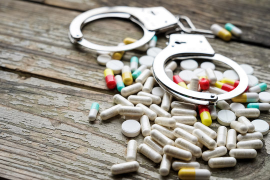 Handcuffs and pills and drugs on wooden table.