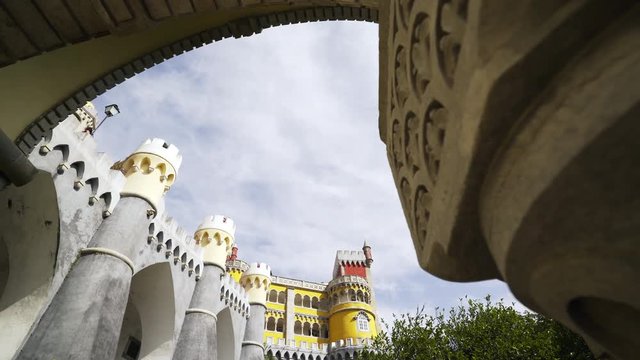Panning shot facade of palace Pena through arch of main gate. Wall decorated towers and custle in suny day at blue sky background. Sintra, Portugal