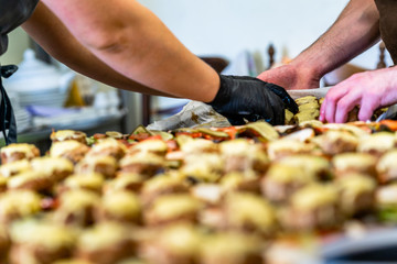 Female and Male Chef Putting Ingredients of Burgers on a Sliced Bread Spread on a Table in Black Gloves