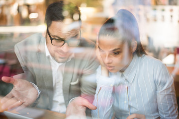 Team of two young and successful business people and designers discussing a project looking at laptop. View from window. Modern businessman and businesswoman working together concept.