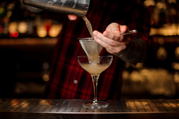 Barman pouring juicy alcoholic cocktail from shaker into cocktail glass