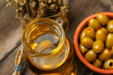 Olives with paprika in a retro style ceramic bowl, twig of dried basil and pitcher with olive oil. Old rustic wooden table.