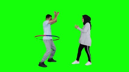 Happy young couple playing hula hoop in the studio. Shot in 4k resolution with green screen background - Powered by Adobe