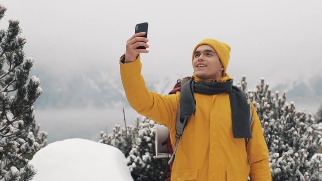 Beautiful mountains in winter time. Man with beard, wearing yellow winter clothes take selfie against the background of beautiful mountains and mountain lake
