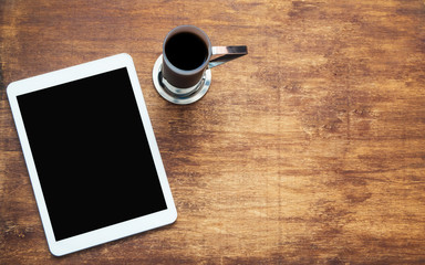 Obraz na płótnie Canvas Touch tablet and cup of coffee on wooden desk. Black blank space on the screen. Mock up