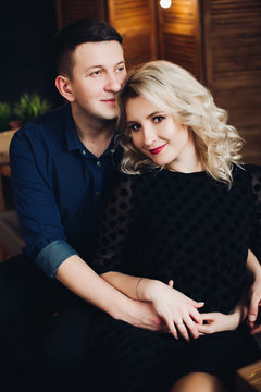 Portrait of sensual and happy couple, hundsome man embracing his charming and pretty blonde woman. Boyfriend touching hair of girlfriend and girlfriend looking at camera and smiling.