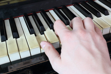 A right hand playing a G (SOL) major chord on an old black piano with yellowed cracked keys, pressing the G (SOL), B (SI), D (RE) notes