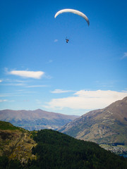 A para glider flying over a big blue lake in the mountains of New Zealand
