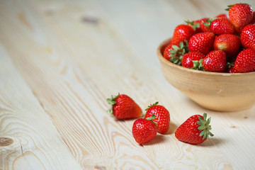 Fresh strawberries in a bowl on wooden table with low key scene.