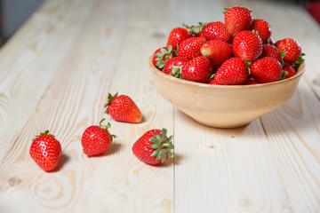 Fresh strawberries in a bowl on wooden table with low key scene.
