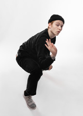 Young freestyle dancer dressed in black jeans, sweatshirt, hat and gray sneakers is dancing in the studio on the white background