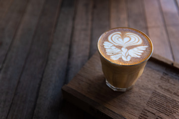 Latte art coffee in glass cup on wooden plate and wooden table