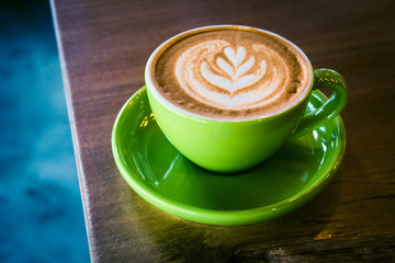 cappucino in a green cup and saucer with foram art in the shape of a leaf