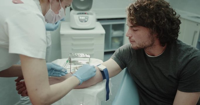 Closeup a charismatic young donor man in a modern clinic was given a blood test , medical assistance was finished the procedure of blood collecting. 4k
