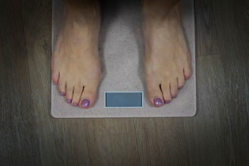 Diet and fitness concept. Close up to female bare feet with pedicure standing on scales with empty display. Woman standing on bathroom scale to check her weight. Weighting. Wellnes and health. - obrazy, fototapety, plakaty
